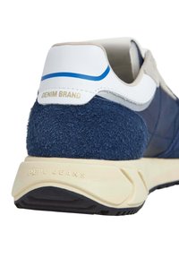 Tênis azul-marinho com calcanhar em camurça texturizada, detalhes em branco e bege claro, e sola em creme. Apresenta os rótulos "DENIM BRAND" e "PEPE JEANS".