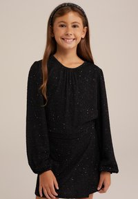 Svart klänning med långa puffärmar som har en texturerad tyg och flerfärgade prickar, kompletterad med ett matchande hårband.