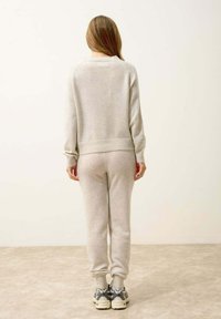 Jasnoszary, miękki sweter z dzianiny i dresy, z prążkowanymi mankietami i pasem. W komplecie sportowe sneakersy z masywną podeszwą.