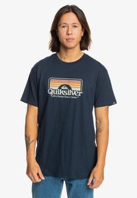 Navyfarbene Baumwoll-T-Shirt mit einem Quiksilver-Logo in Retro-Farben und dem Slogan "Das Leben ist besser Down Under" darunter. Kurze Ärmel.
