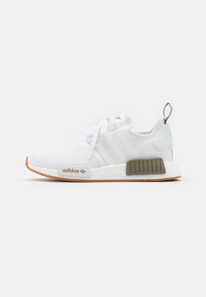 Basket blanche Adidas NMD avec tige en maille, semelle en gomme, accents gris sur la semelle intermédiaire et lacets blancs, montrée de profil sur un fond uni.