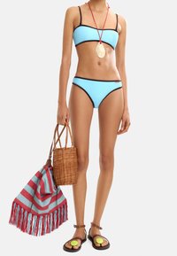 Jasnoniebieski bikini z czarnymi wykończeniami, połączony z brązowymi sandałami na ramiączkach z zielonymi akcentami. W komplecie pleciona torba i pasek plażowy w paski.