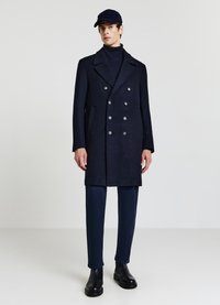 Cappotto doppiopetto color navy in tessuto morbido con bottoni argentati, abbinato a un dolcevita e pantaloni navy, completato da stivaletti neri.