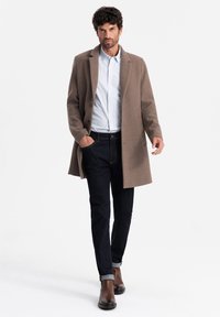 Brun uldfrakke med lige snit, knaplukning, båret over en lyseblå stribet skjorte og mørke jeans, parret med brune læderstøvler.