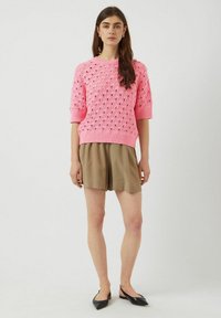 Pull en tricot rose avec un motif ajouré, manches courtes, ourlet côtelé. Associé à un short khaki et des ballerines noires à bride arrière.