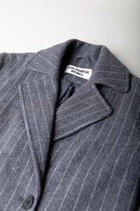 Un sacou gri cu dungi fine, cu guler tăiat și un singur nasture. Prezintă o textură de țesătură moale și o etichetă interioară pe care scrie "COLOURFUL REBEL."