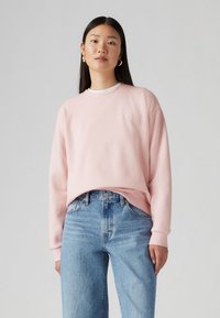Sweatshirt rose clair avec un col rond, coupe décontractée et poignets côtelés, associé à un jean en denim bleu taille haute.
