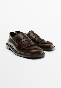 Dark brown leather loafers with fringe detailing and a thick sole, positioned side by side on a white background.