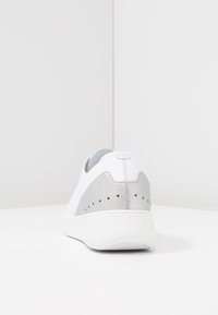 Zapatilla blanca con una parte superior de cuero liso y detalles en gris. Cuenta con un cuello acolchado, un diseño minimalista y pequeños orificios de ventilación.