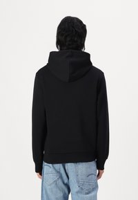 Sudadera negra de tela suave, con capucha ajustable, puños acanalados y dobladillo ceñido. Combina con vaqueros de un azul claro.