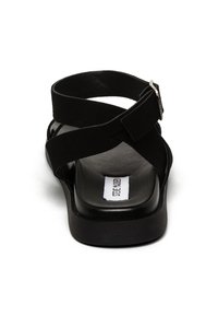 Sandalo nero con fasce incrociate, tacco piatto e texture opaca. Include un dettaglio con fibbia argentata e una soletta con logo.