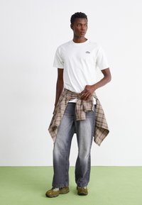 White T-shirt with a small logo, gray plaid shirt tied at the waist, faded gray jeans, and brown sneakers. Simple, casual design.