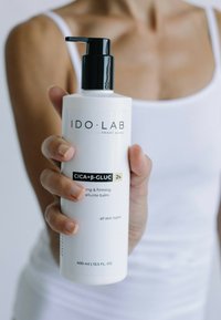 Weiße Flasche mit schwarzem Pumpspender, beschriftet "IDO.LAB CICA+β-GLUC 2%". Straffender Balsam, Größe 400 ml, für alle Hauttypen. Einfaches und modernes Design.