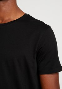 T-shirt noir à manches courtes en coton doux, avec un col rond et une texture lisse sans motifs ni accents visibles.