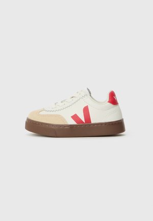 Hvite lærsneakers med beigefarget semsket tupp, rød logoaccent, brun gummisole og teksturert søm rundt kantene.