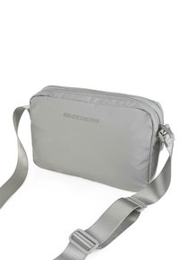 Bolso bandolera gris de Skechers, hecho de material sintético suave, que presenta un cierre con cremallera, correa ajustable y una forma rectangular simple.
