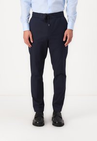 Navy blå, avsmalnede bukser med elastisk liv og snøring. Laget av et glatt stoff, med sidelommer og slim fit.