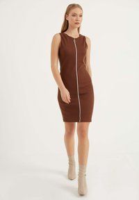 Braunes, geripptes, ärmelloses Kleid mit einem Reißverschluss auf der Vorderseite und taillierter Form, ergänzt durch neutrale Knöchelstiefel.