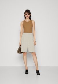 Barna ujjatlan felső, világosszürke, szabott sort, fekete mules cipők és egy sötét táska. Simaság és strukturált formák. Egyszerű vizuális elemek.