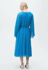 Rochie vaporoasă de culoare albastră, confecționată dintr-un material transparent, cu mâneci lungi, fustă plissată și talie strânsă, cu adunări subtile în jurul gâtului.