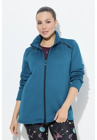 Tyrkysová fleecová bunda s vysokým límcem, zapínáním na zip a kontrastními černými švy. Kombinováno s legínami s nebeskými vzory.