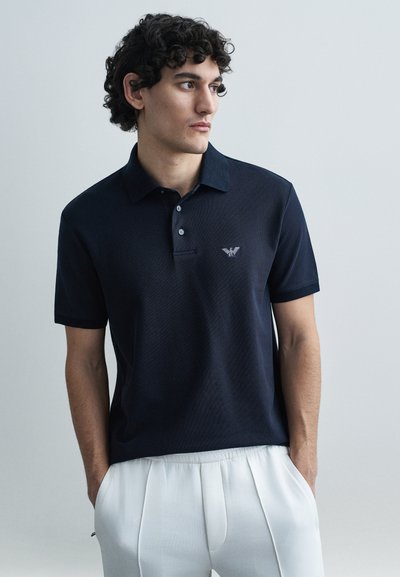 Navyblauw poloshirt van gestructureerde stof met een kraag, korte mouwen en drie knopen. Heeft een klein logo op de borst.
