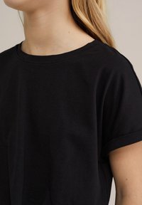Sort kortærmet t-shirt med rund halsudskæring og oprullede manchetter, lavet af blød bomuld. Stoffet har en glat tekstur og en tætsiddende silhuet.