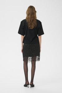 Zwart topje met korte mouwen, gecombineerd met een zwarte, met pailletten versierde rok met een doorschijnende overlay. Zwarte panty's en schoenen met hak maken de outfit compleet.