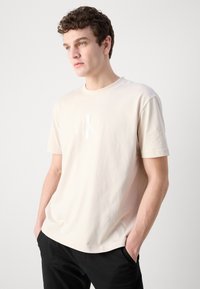 Light beige cotton T-shirt featuring short sleeves and a crew neck, with a subtle CK logo printed in a slightly lighter shade.