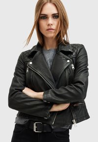 Svart lädermotorcykeljacka med quiltad axeldesign, silvriga dragkedjor och figursydd passform. Kombinerad med en grå tröja under.