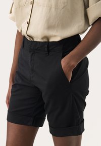 Svarta bomullsshorts med avslappnad passform, uppvikta fållar, sidfickor och platt midjeband. Slät textur och minimala sömdetaljer.