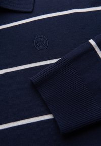 Marineblauer Strickpullover mit weißen horizontalen Streifen, gerippten Bündchen, Kragen und einem bestickten runden Logo mit dem Buchstaben Q.