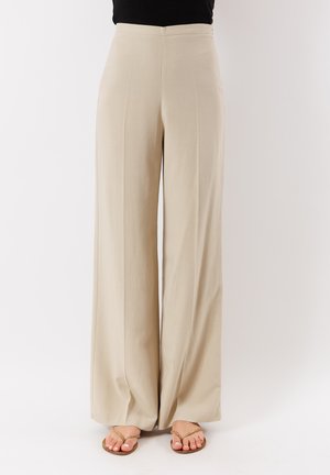 Pantaloni beige a gamba larga in tessuto leggero, con vita alta e pieghe frontali, abbinati a sandali piatti color nocciola.