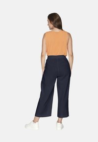 Apelsinfärgad ärmlös topp och marinblå culotte-byxor med elastisk midja. Skorna är vita med en slät yta.
