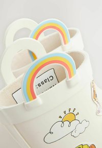 Sac seau blanc avec des poignées en forme d'arc-en-ciel, orné d'autocollants colorés de nuages et d'un soleil. Texture lisse et design arrondi.