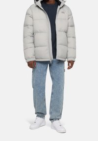 Jasnoszara kurtka puchowa z kapturem, zamkiem błyskawicznym i elastycznymi mankietami. Nosi się ją na granatowej bluzie i łączy z jasnoniebieskimi dżinsami oraz białymi trampkami.
