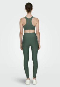 Olive green sports bra and high-waisted leggings, both made from stretchy material. Leggings have seamless design and minimalistic branding.