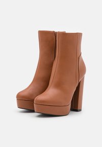 Paire de bottines plateformes en cuir marron avec hauts talons carrés et fermetures éclair latérales sur fond blanc.