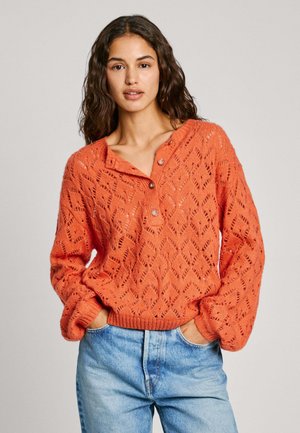 Oranz värvuse kudum, millel on teemantmuster, henley-kaelusega ja kahe nööbiga. Kombineeritud siniste denimitehnikatehnustega.