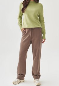 Grüner gestrickter Pullover mit hohem Kragen, kombiniert mit braunen Hosen mit Kordelzug. Das Outfit hat gerippte Bündchen und eine lockere Passform.