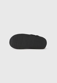 Suela de un zapato negro con suela de goma acanalada sobre un fondo gris claro liso.
