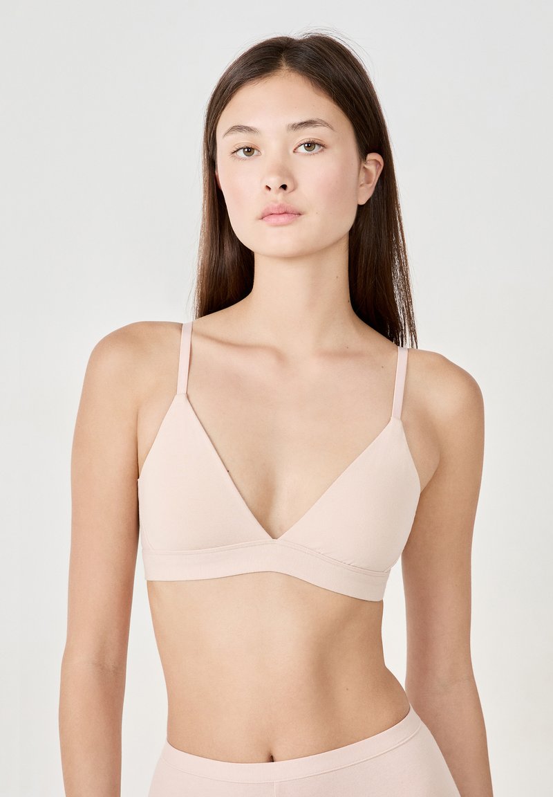 Bralette de couleur rose clair, sans couture, en forme triangulaire, avec des bretelles fines et réglables, et une large bande sous-poitrine. Texture de tissu douce, design minimaliste.