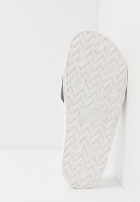 La suela de las chanclas Levi's está hecha de un material de goma blanca con un patrón de espiga, grips circulares y un logo en relieve en el centro.