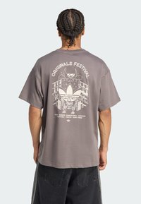 Gray oversized t-shirt, cotton material, features a graphic design on the back with "Originals Festival" text and city names.