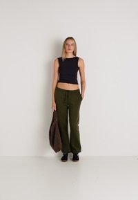 Čierny crop top, olivovo zelené nohavice so širokými nohavicami, hnedá taška, čierne topánky. Jednoduchý dizajn so zameraním na pohodlie a neformálny štýl.