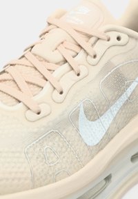 Μπεζ αθλητικό παπούτσι Nike Air Max με ροζ κορδόνια, υφασμάτινη υφή και ορατή αερόσολα στη σόλα.