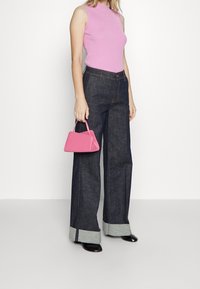 Rosa ribbad ärmlös topp, mörk denim vida byxor med vikta grå fållar, och en liten rosa handväska i triangulär form.