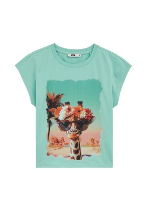 Maglietta turchese chiaro con grafica di una giraffa che indossa occhiali da sole e una corona di fiori, in piedi in un paesaggio tropicale con palme.