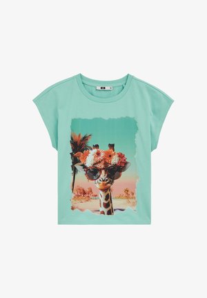 Maglietta turchese chiaro con grafica di una giraffa che indossa occhiali da sole e una corona di fiori, in piedi in un paesaggio tropicale con palme.