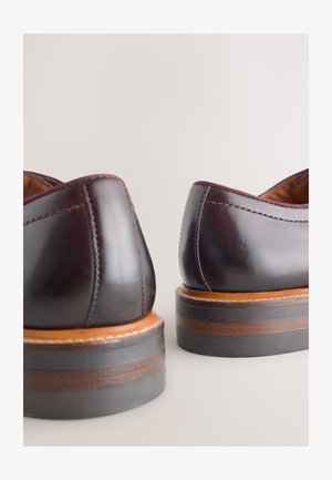 Dark burgundy leather shoes with a smooth finish, contrasting wooden soles, and subtle stitching along the edges. Rounded heel design.